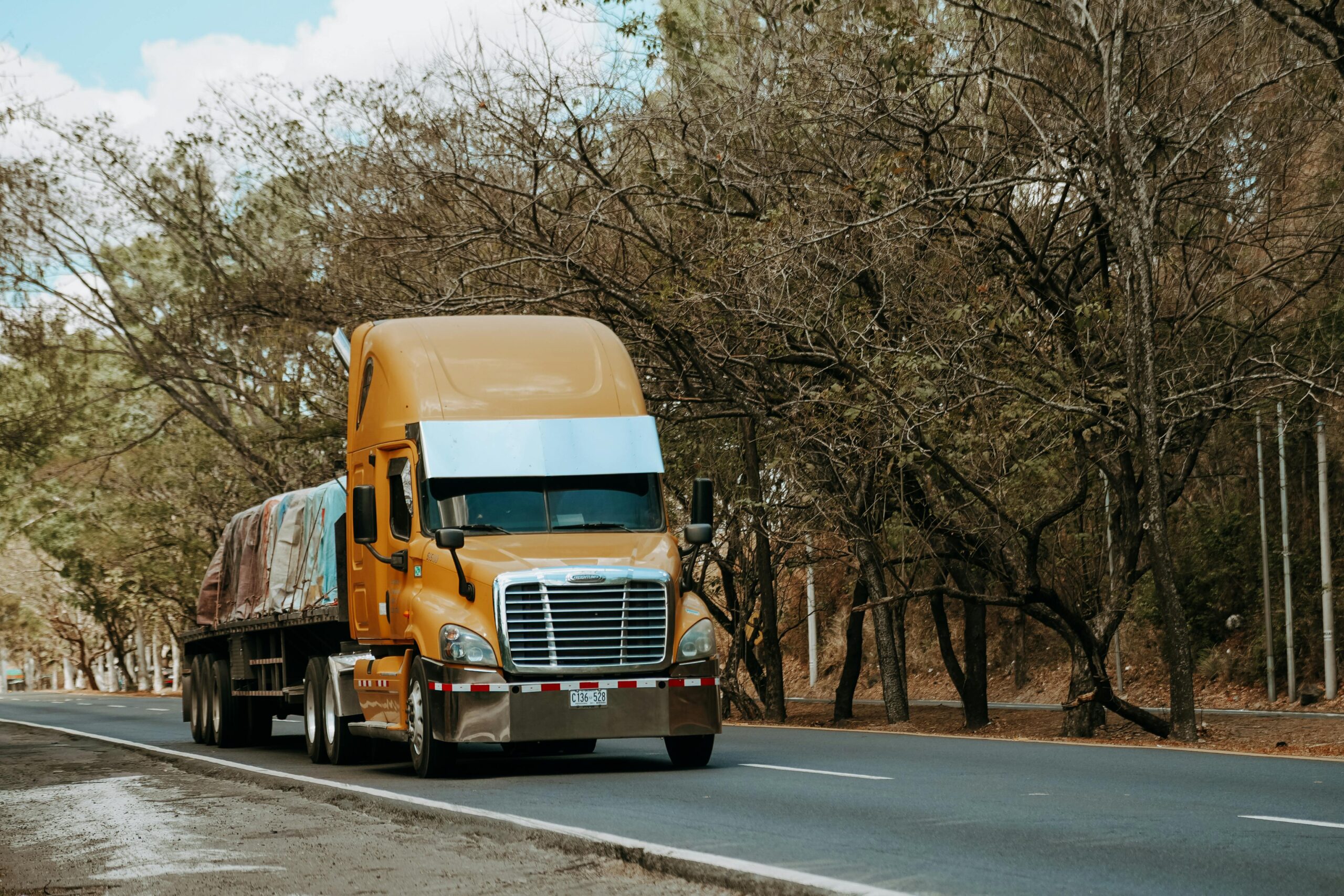 Orange semi-truck driving on highway through trees