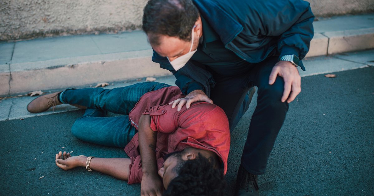 Masked man helping unconscious person lying on sidewalk